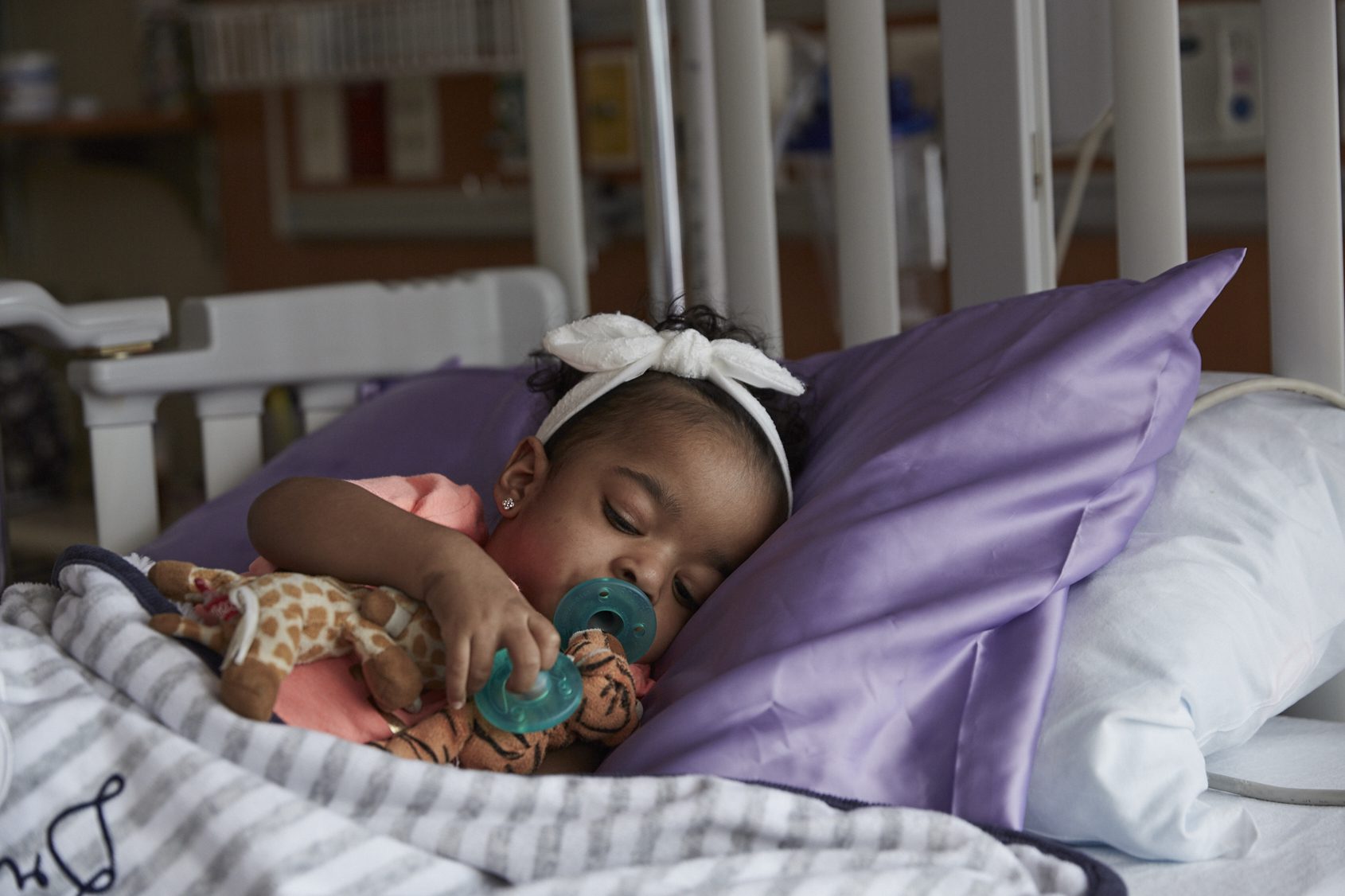 A baby with a pacifier asleep and snuggling a small stuffed animal