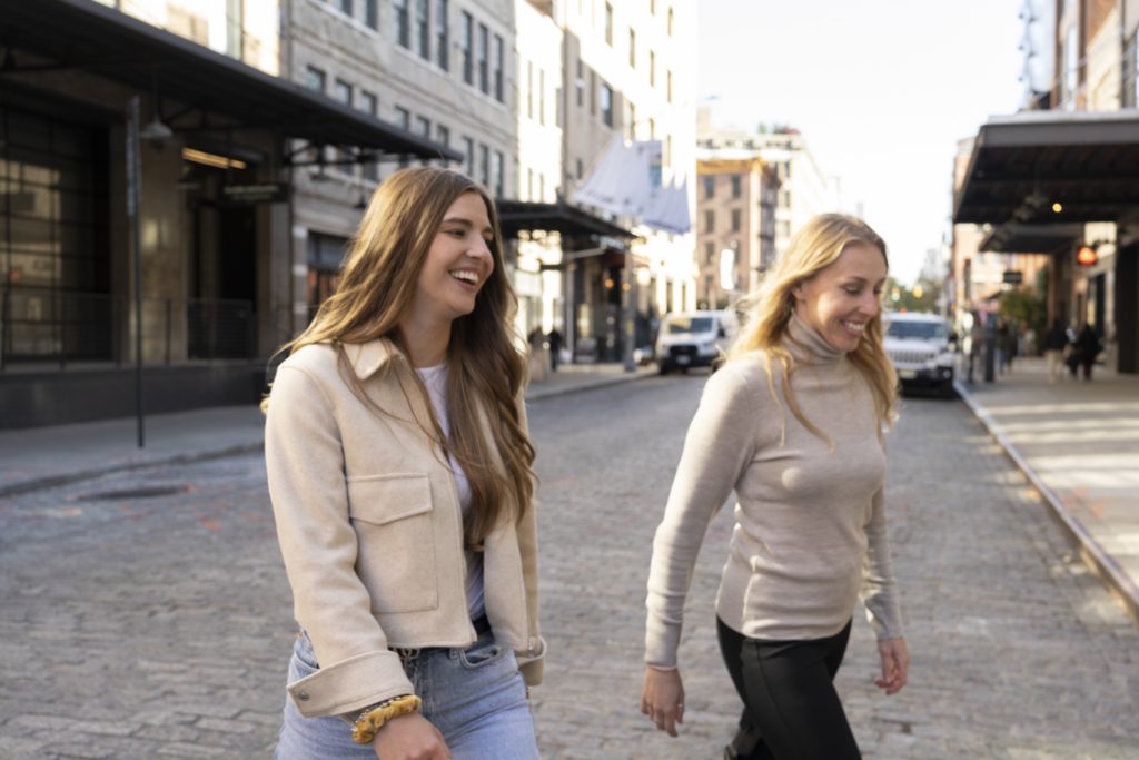 two women smiling side by side while crossing a cobblestone street